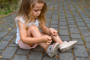 A little girl puts a band-aid on a wound on her knee after an accident. Selective focus.
