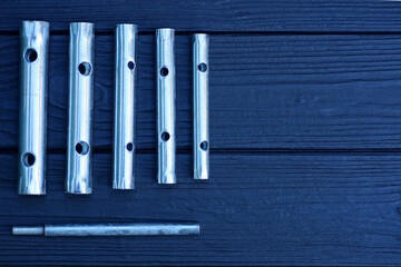 a set of a row of gray metal tubular wrenches lie on a black wooden table