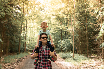 Happy Family father gives son a piggyback walking in the woods enjoying adventure exploring nature 