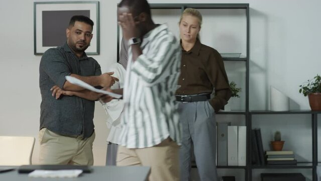 Group of three multi-ethnic managers standing in office staring at their Black colleague walking by mocking him