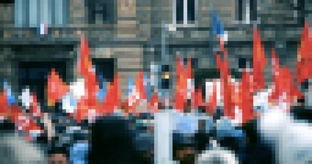 Pixelated protest in city center with people holding red flags.