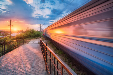 High speed train in motion on the railway station at sunset in summer. Moving modern intercity passenger train, railway platform, green trees and sunlight. Railroad in Urkaine. Railway transportation - obrazy, fototapety, plakaty