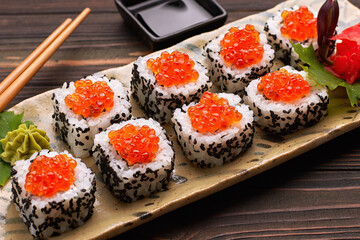 Sushi roll with red caviar on a plate with wasabi, ginger, maple leaves and chopsticks for sushi, on a wooden background. Close up