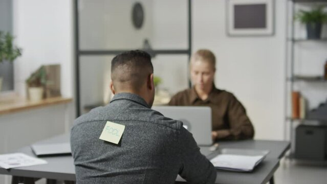 Selective focus shot of young African American bully sticking paper with insulting word on his colleagues back