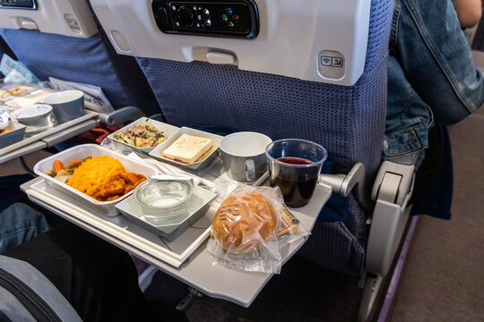 Inflight airplane Asian food set meal served consisting rice and spicy chicken, appetizer, dessert, bun and red wine