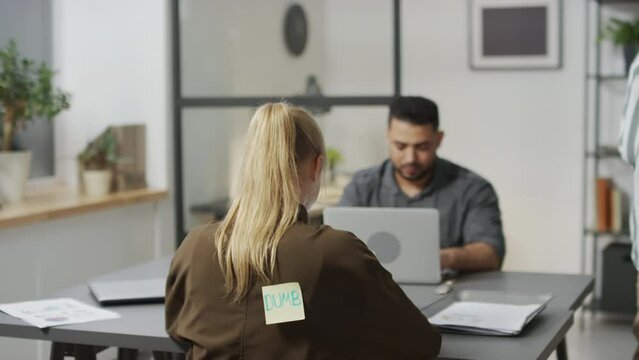 Selective focus shot of cheeky African American bully sticking paper with offensive word on his female colleagues back