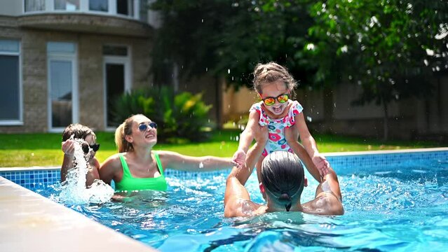 Happy parents and two kids are swimming in the pool and dad throwing his daughter in the air. Slow motion
