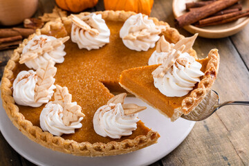 Traditional pumpkin pie topped with whipped cream with a slice taken out