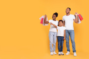 Naklejka premium Family shopping. Happy parents and son with colorful bags on orange background, space for text