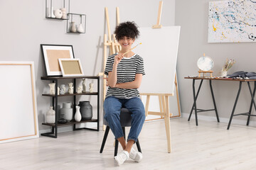 Young woman with brush palette near easel in studio