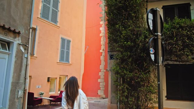 Beautiful girl in a dress walking to the colorful old tower clock in Saint Tropez village. Young woman visits the Famous tourist destination in Cote d'Azur, France with a church tower.