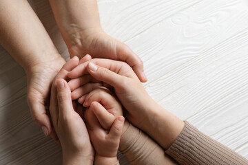 Family holding hands together at white wooden table, top view. Space for text