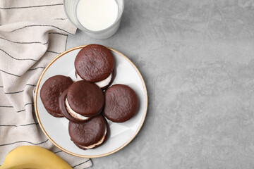Tasty sweet choco pies, glass of milk and banana on light gray table, flat lay. Space for text