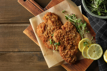 Tasty schnitzels served with lemon and microgreens on wooden table, flat lay. Space for text