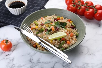 Tasty fried rice with vegetables served on white marble table, closeup