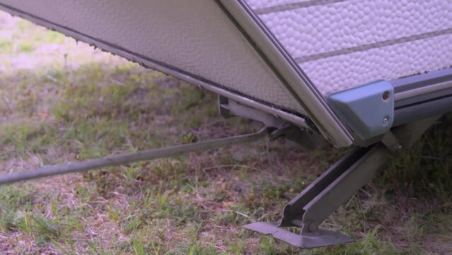 A steel lever rotating to uninstall a part of the caravan parked outside. Caravan leaving the campsite. The camera zooms out.