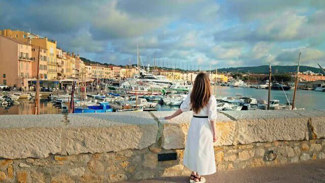 Beautiful girl enjoys the view of Port de Saint-Tropez with boats and ships, coastal town on the French Riviera. Saint-Tropez picturesque, cafe and shop-lined harbor and luxury yacht destination.