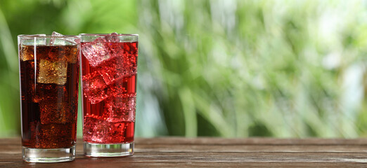 Tasty refreshing soda drinks with ice cubes on wooden table outdoors. Banner design with space for...