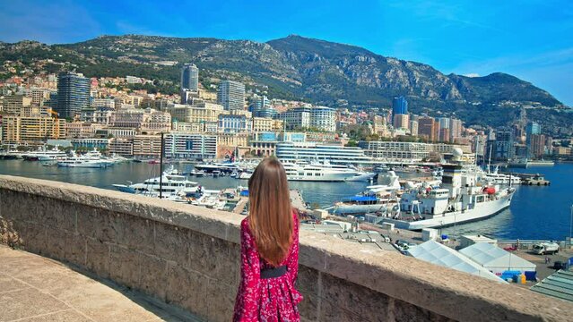 Beautiful girl looking at Port Hercule with Monaco's buildings in background. Young woman enjoys the view of luxury ships, yachts, and deep-water port in the South of France, French Riviera.
