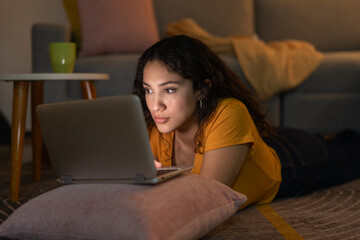 Young woman using laptop, lying on living room floor