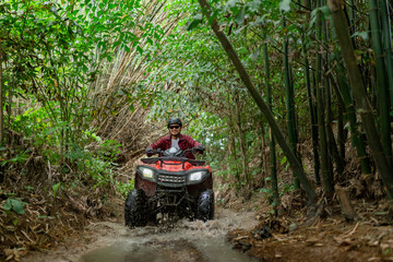 Asian guy having fun while driving an atv in the jungle alone. Drive through water in the deep forest. © 2B
