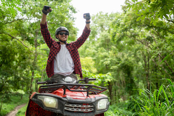 Asian guy having fun while driving an atv in the jungle alone. Raised hands, smiling and happy.