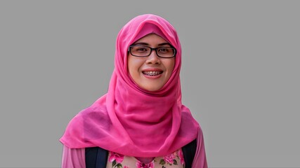 Close up portrait of young Muslim woman wearing pink hijab and dress with eyeglasses. Smiling and happy expression.