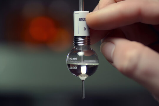 Extreme close-up of a pH meter electrode tip showing a glass bulb that measures the pH level of a solution with a hand holding the meter in the background.