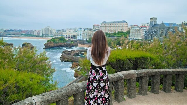 Beautiful girl in a dress taking pictures of the elegant seaside town Biarritz. A model woman photographing a European royalty resort town in the south of France, Basque coast.