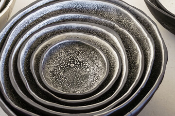 A close-up of a set of nested handmade organic clay bowls with black and white speckled glaze