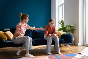 Conflict between parent and teenage. Teen girl sitting on sofa ignoring toxic mother scolding...