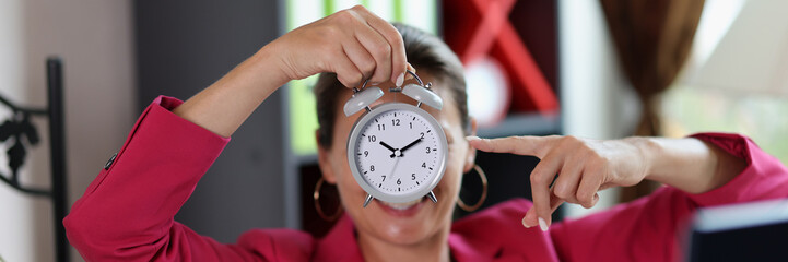 Woman in office points to alarm clock in her hand.