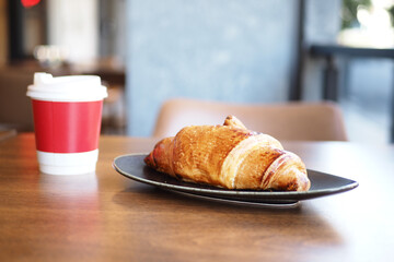 fresh baked croissant and paper coffee cup on table 