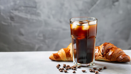 Cold black coffee with ice cubes in tall glass and fresh croissant. Refreshing coffee drink on a...