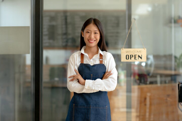Young Asian business owner looking at camera with open sign.
