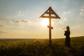 woman prays in front of a Christian cross at sunset. silhouette Christian woman praying at nature.