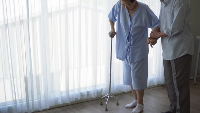 Asian elder senior husban help wife practice walking use stick physical theraphy to recover leg injure
