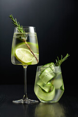 Gin tonic with ice, rosemary, lime, and cucumber in frosted glasses.