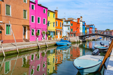 Fototapeta na wymiar Picturesque colorful idyllic scene with a boats docked on the water canals in Burano Venice Italy. Water reflection.