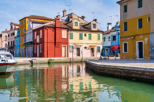 Picturesque colorful idyllic scene with a boats docked on the water canals in Burano Venice Italy. Water reflection.