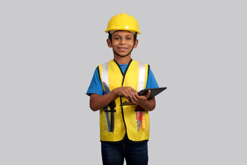 Indian Asian kid boy aged 7 to 8, wearing a yellow helmet and Safety jacket. holding tablet in hand. He had a dream to future study as an engineer. He smiled happily, Concept little engineer