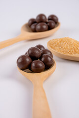 Chocolate balls on wooden spoon and brown sugar on wooden spoon on white background.