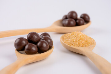 Chocolate balls on wooden spoon and brown sugar on wooden spoon on white background.