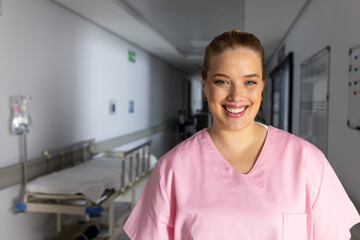 Portrait of happy caucasian female doctor wearing scrubs in corridor at hospital, copy space