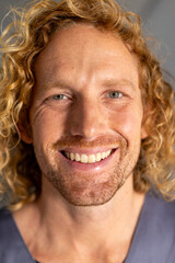 Portrait of happy caucasian male doctor with curly hair in corridor at hospital