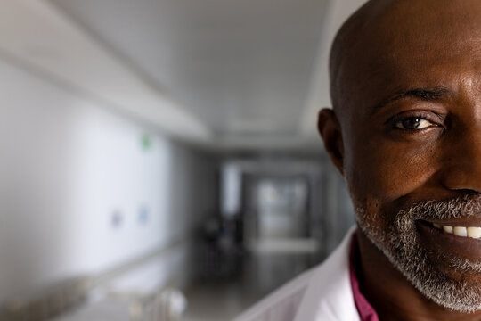 Portrait of happy african american male doctor wearing lab coat in corridor at hospital, copy space