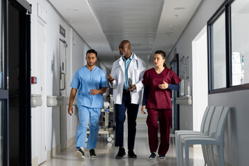 Diverse doctors discussing work and walking through corridor at hospital