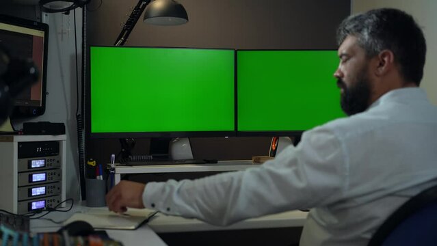Man Trader or Businessman Works at Desktop Computer with Two Monitors with Green Screen Mock-up