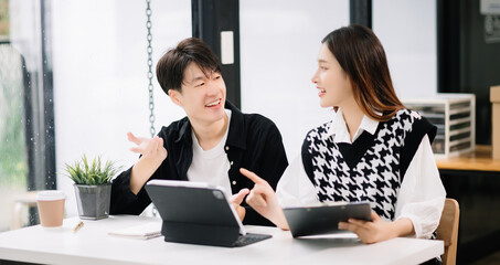 Asian business colleague business presents and explains and using laptop and tablet. Teamwork, financial marketing team, while sitting in modern office room..