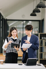 Asian business colleague business presents and explains and using laptop and tablet. Teamwork, financial marketing team, while sitting in modern office room..